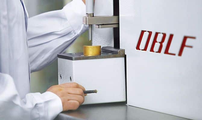 A scientist operating an OBLF spectrometer to analyze a metal sample.