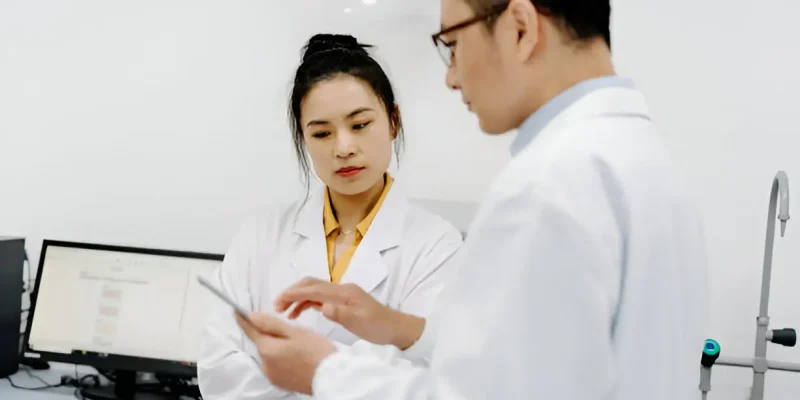 Two professionals discussing data on a tablet in a clinical lab.